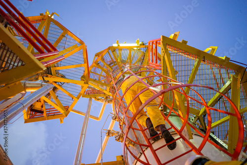 Принти на полотні Low angle view of oil worker in coverall and helmet on an industrial steel ladder with safety cage