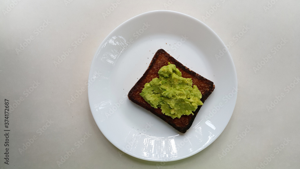 Baked toast with avocado on a white plate. Vegan food. Vertical photo