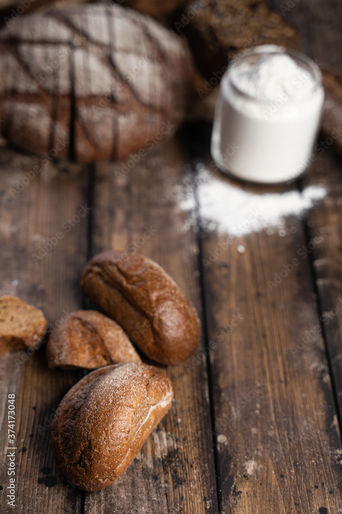 From above fresh rye buns placed on wooden table near loaf of bread and jar of flour in rustic kitchen From above fresh rye buns placed on wooden table near loaf of bread and jar of flour in rustic kitchen