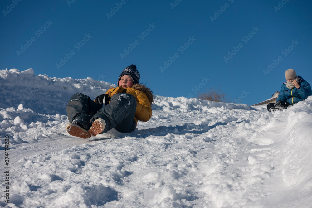 happy boy sliding down snow hill on sled outdoors in winter, sledging and season concept