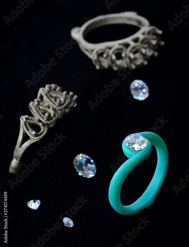 Round diamonds placed on the mold, green wax rings and several silver metal molds placed on a black floor.