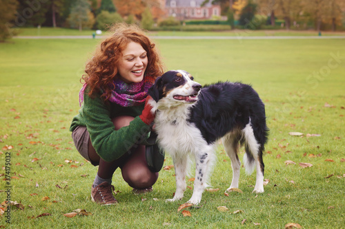 jeune et jolie femme rousse dans un parc arboré en automne avec des feuilles mortes promenant un grand chien en laisse 