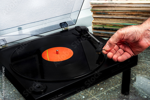 Fotografija hand placing a vinyl record on a record player with a stack of vinyls behind