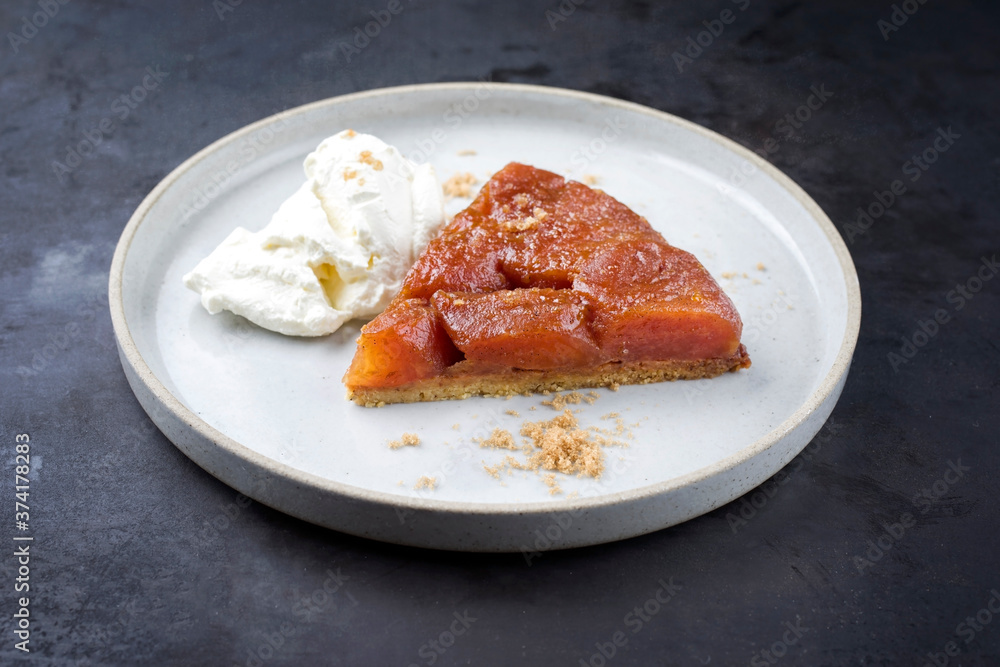 Traditional French tarte tatin with apples and ice cream offered as close-up on a modern Nordic design plate with rustic background Traditional French tarte tatin with apples and ice cream offered as close-up on a modern Nordic design plate with rustic background