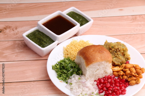 Dabeli is an Indian snack item served with Pomegranate Seeds and Cilantro in white ceramic plate. with green chutney and tamrind chutney. photo