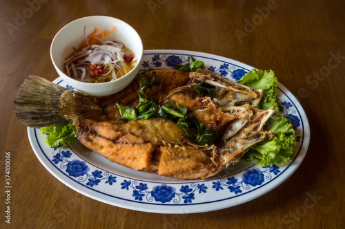 Fried sea bass fish in white plate with spicy and sweet sauce in Thai style . crispy Thai style deep fried whole sea bass fish served with spicy mango sauce. crispy deep fried sea bass 