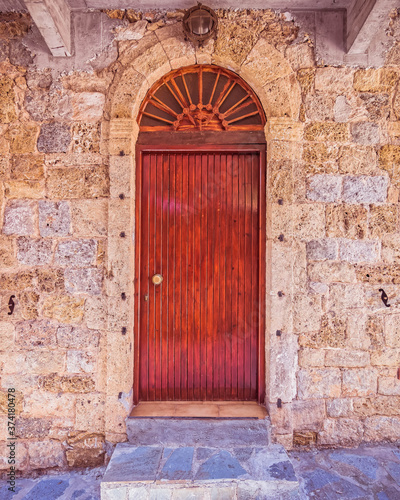 stone wall house natural wooden arched door by the sidewalk © Dimitrios