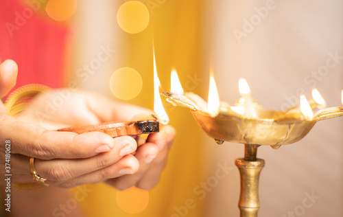 Closeup of woman hands lighting lantern diya or Lamp during festival ceremony - concept of traditional Indian festival and ritual celebrations. photo