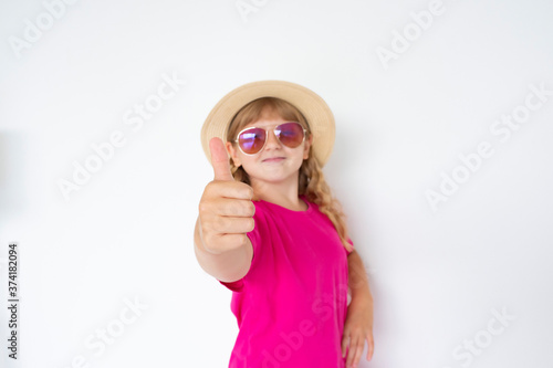 teenage girl in a hat, sunglasses and a bright pink T-shirt happily shows a thumb up. the face is blurred.