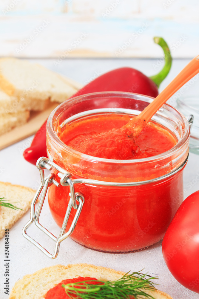 Ajvar, pepper mousse in a jar and on gray plate with bread and gray backgground Ajvar, pepper mousse in a jar and on gray plate with bread and gray backgground