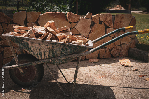 Wheelbarrow with orange slate stones on wall background, rock material for wall renovation on construction site