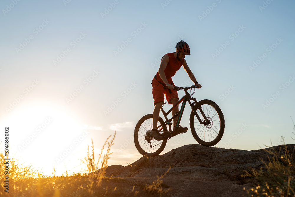 The cyclist rides on the rocks on a mountain bike, in the background of a sunset, a copy of the free space.