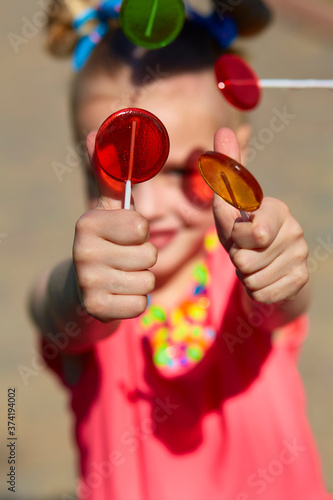 vertical frame portrait of a girl she stretched out her arms forward and showed a gesture class and holds lollipops in her hands. photo in the park. the bright sun is shining. summer