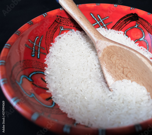 Primer plano de granos de arroz blanco sin cocinar dentro de un tazón de cerámica rojo aislado sobre un fondo negro. Luz selectiva y foco selectivo sobre los granos de arroz.  photo