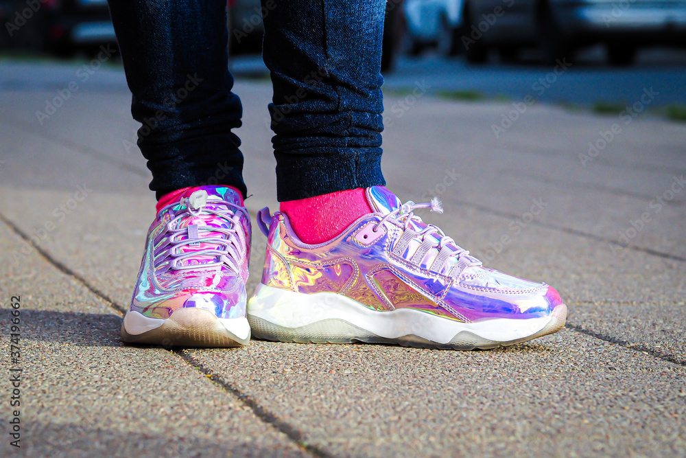 Purple holographic sneakers on a girl legs, with city in the background, selective focus