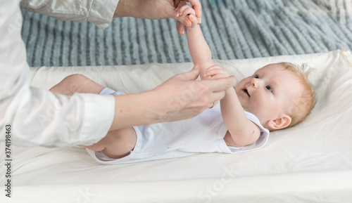 The nurses hands are doing gymnastics for a beautiful baby in a white bodysuit