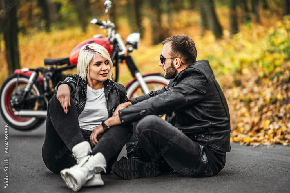 Pretty couple near red motorcycle on the road in the forest with colorful blured background Pretty couple near red motorcycle on the road in the forest with colorful blured background