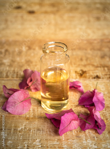 Close-up of essential oil in a small glass bottles with bougainvillea flowers on wooden background. Selective focus and copy space for text. Portrait format

