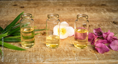 Essential oil in three small glass bottles with bamboo leaves, bougainvillea and frangipani flowers on wooden background. Selective focus and copy space for text. Natural cosmetics. 