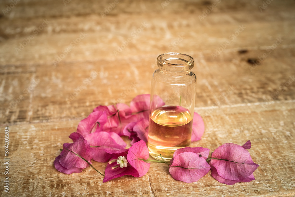 Close-up of essential oil in a small glass bottle with bougainvillea flowers on wooden background. Selective focus and copy space for text. Natural cosmetics. Close-up of essential oil in a small glass bottle with bougainvillea flowers on wooden background. Selective focus and copy space for text. Natural cosmetics.