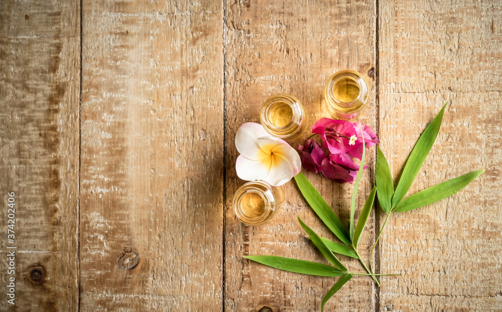 Essential oil in small glass bottles with bamboo leaves, bougainvillea and frangipani flowers on wooden background. Selective focus. top view and copy space for text. Natural cosmetics.
