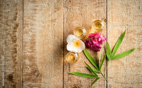 Essential oil in small glass bottles with bamboo leaves  bougainvillea and frangipani flowers on wooden background. Selective focus. top view and copy space for text. Natural cosmetics. 