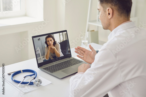 The doctor is giving an online consultation from his medical office. The male doctor is using a laptop and listening to his patient.