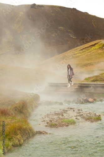 Girl walks down the stairs into the steamy waters of a hot spring river in Iceland