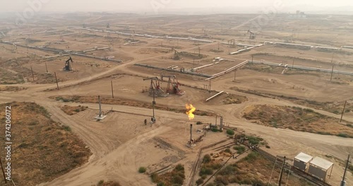 Gas flare coming out of a flare stack in California, vast oil fields with pipelines transporting oil from oil pumps, aerial drone shot photo