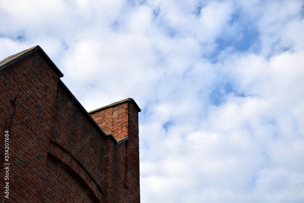 Fragment of a brick wall of a factory building against a background of the blue and cloudy sky.