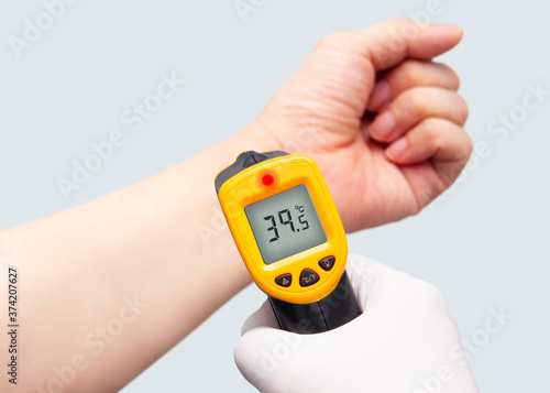 Hand holding a thermometer to check body temperature with latex glove on.