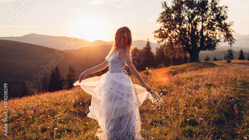Beautiful bride dancing in blue wedding dress in mountains at sunset. Woman holding gown and flowers © maryviolet