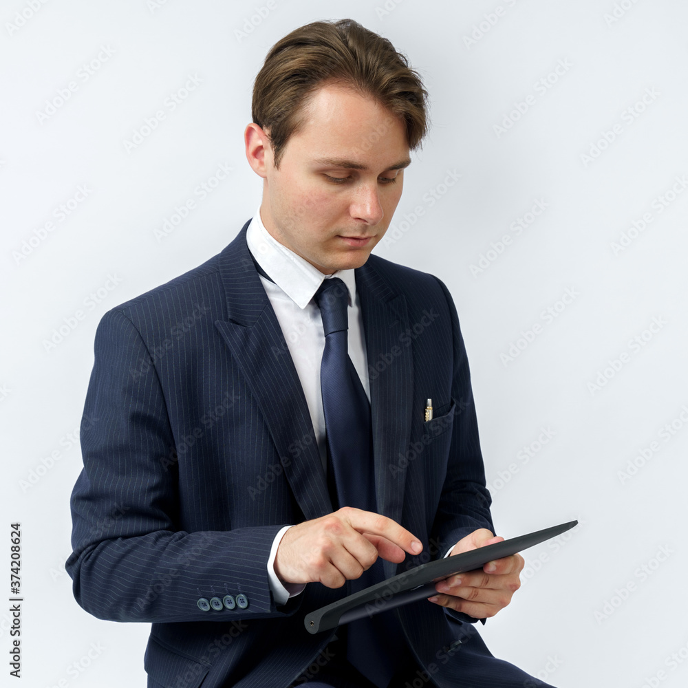 Portrait of a businessman in a blue suit who sits and works with an electronic tablet. White background Portrait of a businessman in a blue suit who sits and works with an electronic tablet. White background