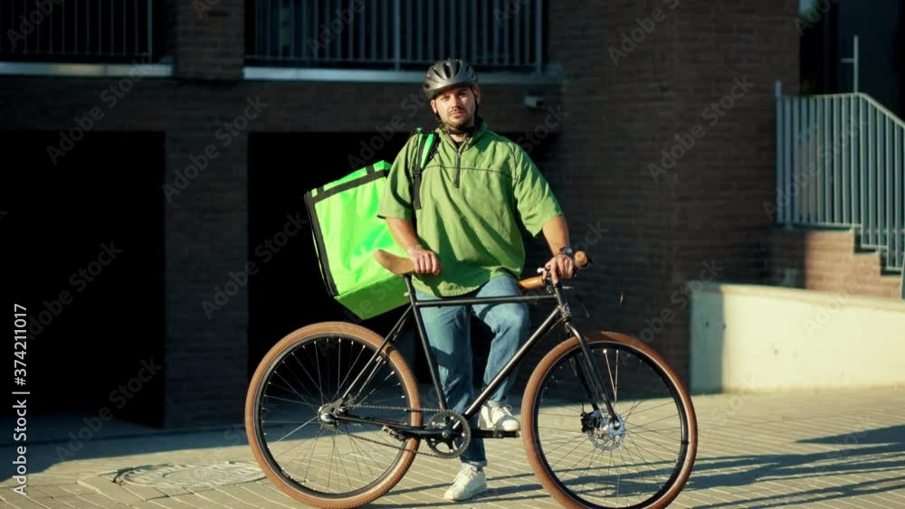 Close up portrait attractive delivery man standing with bicycle backpack looking at camera in city job order courier shipping parcel package slow motion Close up portrait attractive delivery man standing with bicycle backpack looking at camera in city job order courier shipping parcel package slow motion