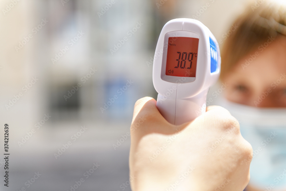 Boy with a facemask have a high body temperature, digital thermometer with  red display indicating fever. New normal, back to school during pandemic  Stock Photo | Adobe Stock