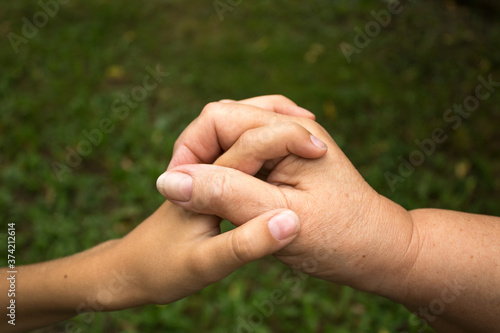 A grandmother and a small child hold hands against a background of green grass. The concept of love and friendship  between generations. International Day of Older Persons and Grandparents Day © DiandraNina