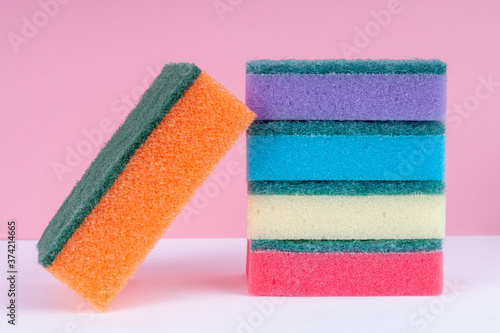 Multicolored sponges for washing dishes on top of each other on a pink background. Cleaning concept.