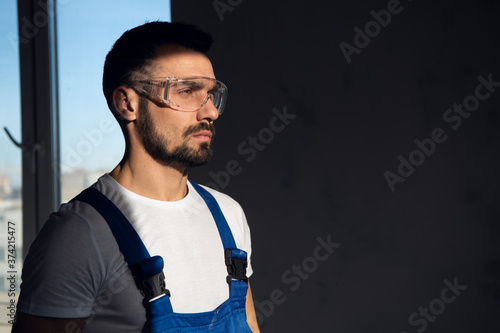 The repairer stands in a dark room. He is wearing blue work clothes