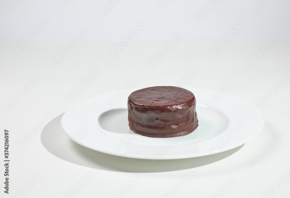 Typical argentinean chocolate alfajor with dulce de leche filling on a white plate on white background Typical argentinean chocolate alfajor with dulce de leche filling on a white plate on white background