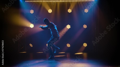 Handsome young man dancing break dance, hip hop, street dancing in studio, isolated. Shot in the studio against a black background with dynamic neon lights. Silhouette. Slow motion.
