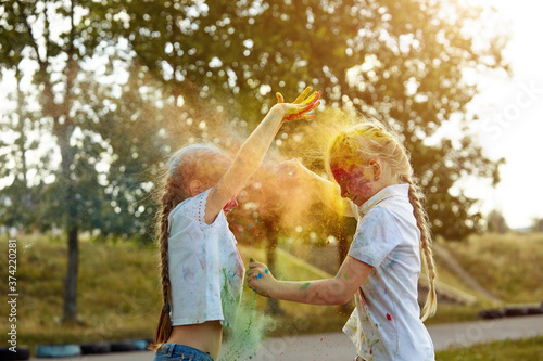 Happy smiling girls have fun using Holi colors, in the summer at sunset. Selective focus