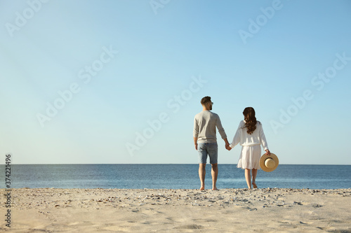Young couple walking on beach near sea, back view. Honeymoon trip