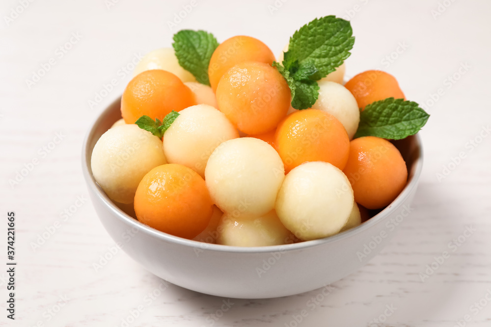 Melon balls and mint in bowl on white wooden table, closeup Melon balls and mint in bowl on white wooden table, closeup