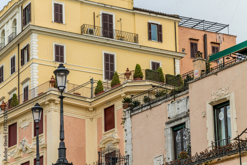 Balconies and windows with potted plants. Beautiful yellow and pink colors with details of houses in Rome, Italy.