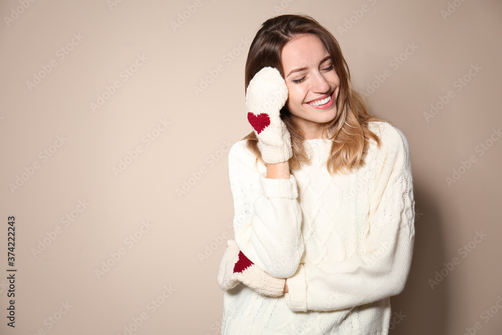 Happy young woman wearing warm sweater and knitted mittens on beige background Happy young woman wearing warm sweater and knitted mittens on beige background