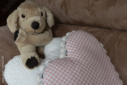 Closeup of a cuddly stuffed animal puppy on a couch with heart pillows