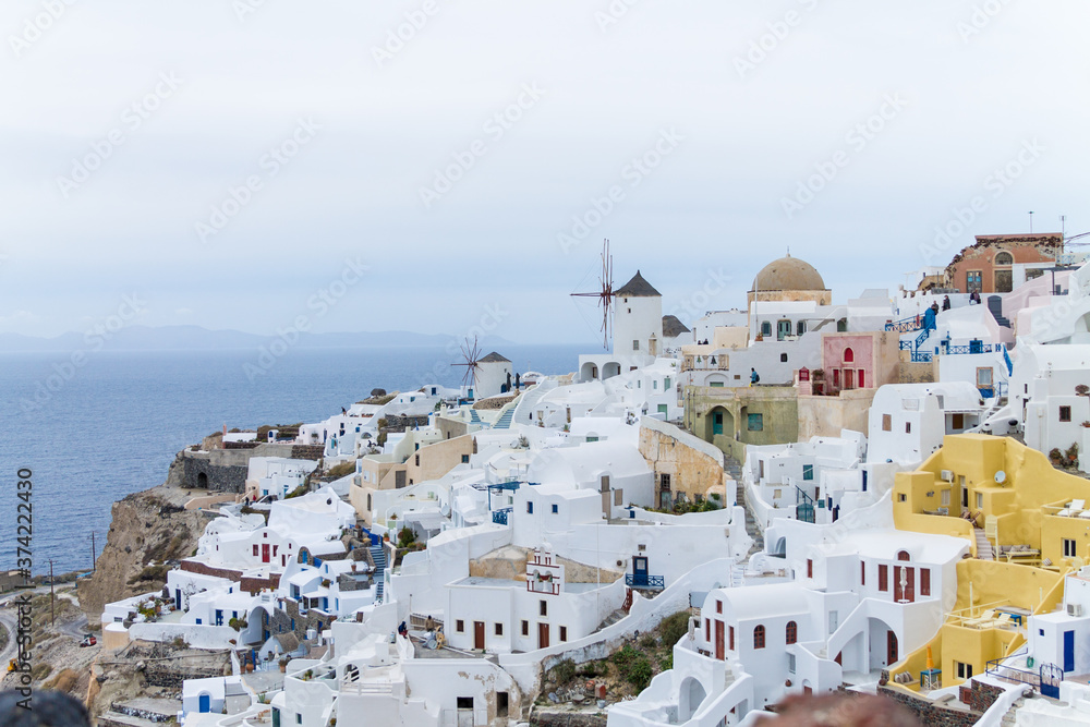 Famous view, old town in Oía, Santorini Island. Beautiful holiday destination. White houses and windmill on cloudy day in Greece.