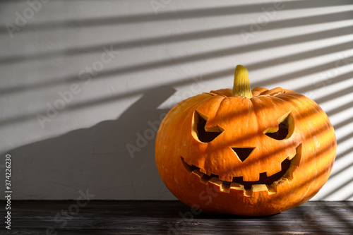 Halloween holiday background. Spooky Halloween pumpkin on the table, illuminated by sunlight through the jalousie. Shadows. Copy space