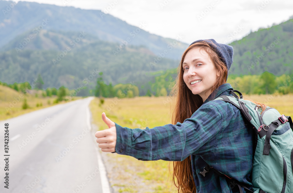 Smiling young woman hitchhiking along a road. Empty space for text