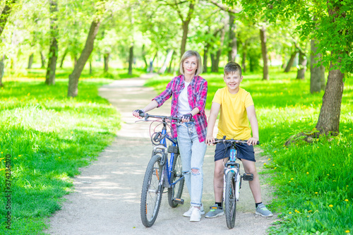 Portrait of mother and son standing with bicycles in sunny summer park. Empty space for text